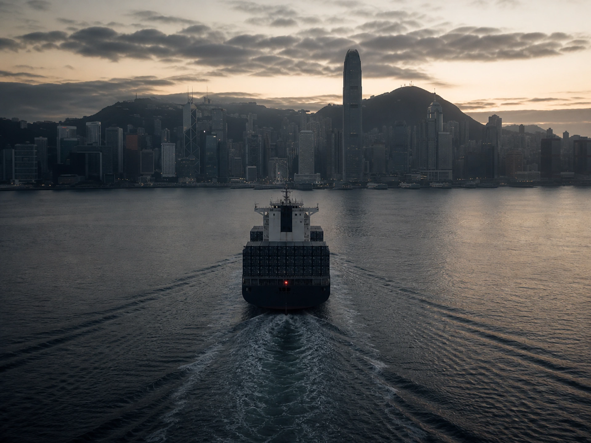 Containerschiff läuft bei Tagesanbruch in den Victoria Harbour ein, dahinter die Skyline Hongkongs